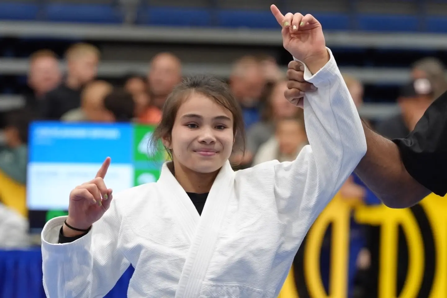 Bailey Heinsohn in a white gi with her hand raised after a jiu-jitsu match win.